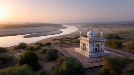 Naklejka premium Serene Sunset Over Historic Structure by Riverbank Surrounded by Lush Greenery and Vast Open Landscape