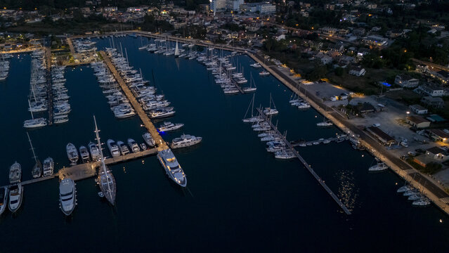 Gouvia, Greece - 26 June 2026: Aerial view of D-Marin Gouvia Marina at night, with yachts and sailboats docked along piers, illuminated waterfront buildings, and calm dark waters.