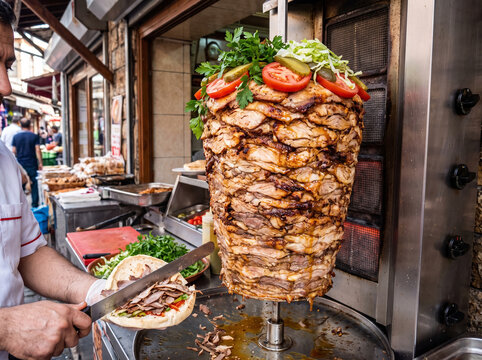 Chef expertly carving delicious doner kebab from a vertical grill on a bustling street showcasing authentic Middle Eastern culinary traditions and savory street food preparation.