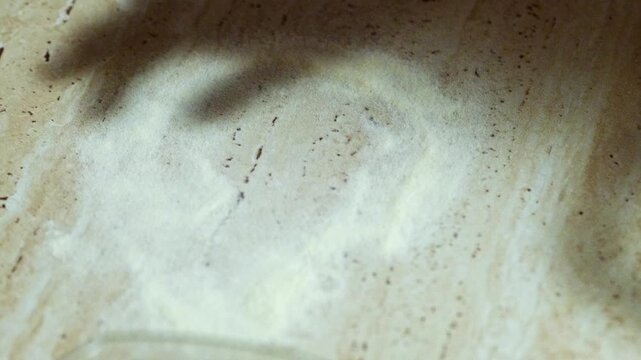 Close up of a hand sprinkling flour onto a wooden board before kneading dough