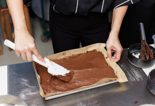 Asian beautiful woman baker pouring cacao liquid dough into baking tray ingredients process preparation of chocolate brownie cake dessert professional bakery fresh homemade recipe kitchen culinary.