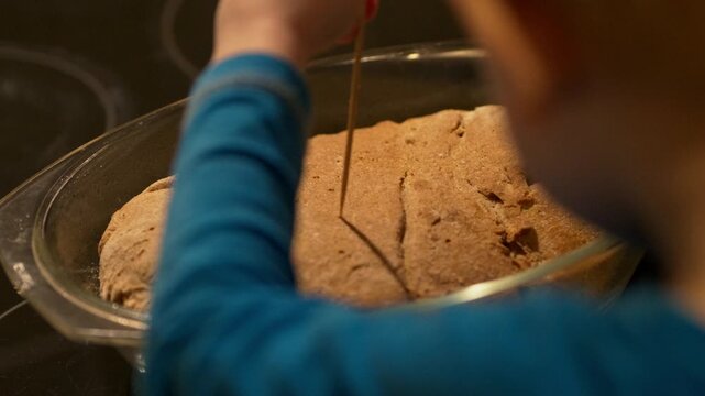 Close up of a little boy poking holes in a freshly baked healthy homemade bread crust with a wooden skewer