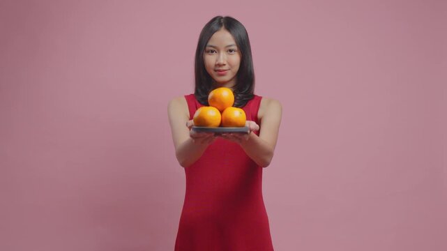 Pretty young Asian woman in a traditional cheongsam dress is giving mandarin oranges.