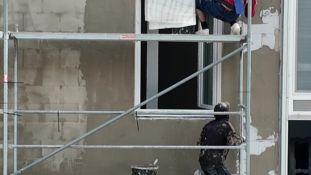 Construction workers applying plaster to building exterior on scaffolding. Skilled laborers meticulously apply plaster to a building's facade while working on scaffolding, showcasing the process of