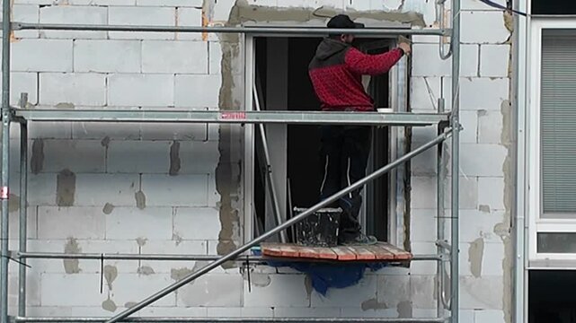 Construction worker applying plaster to a building facade from scaffolding. A worker on scaffolding meticulously applies plaster to a wall, showcasing the building process and exterior renovation work