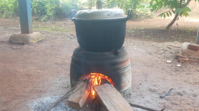 Traditional cooking using a wood burning stove in an outdoor area. A large pot is placed on the stove which is lit by a fire burning wood.