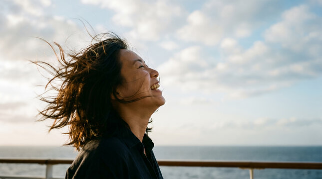 Asian woman laughing in wind by the sea