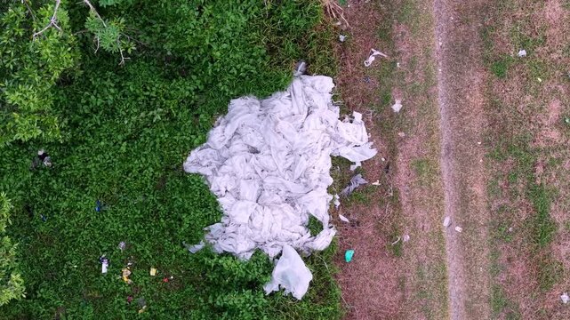 Drone footage shows discarded plastic sheets and scattered litter along grassy edge of a green field.