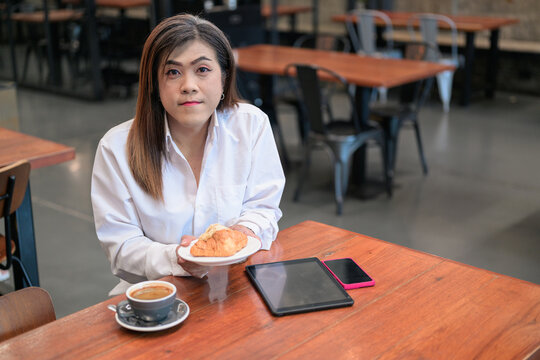 Southeast Asian Transgender Businesswoman Looking at Camera with Croissant and Copy Space
