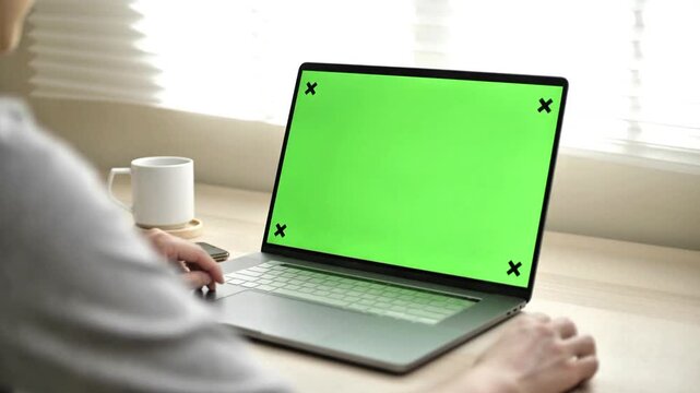 Over the shoulder view of person using laptop with green screen