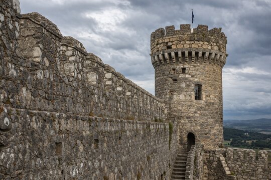 Weathered stone wall and watchtower of medieval castle under cloudy sky.
