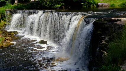 Keila waterfall cascades powerfully over natural rock formations, creating a scenic landscape with lush green foliage and clear flowing water during summer © Dark Artistic