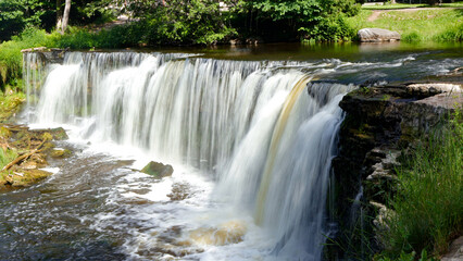 Keila waterfall cascades over a wide rock formation, creating white foamy water in a lush green summer forest and tranquil natural environment © Dark Artistic