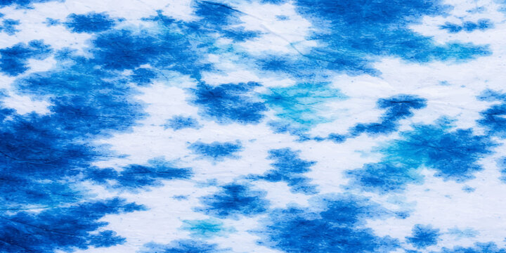 An abstract pattern of blue dye splatters on a white fabric, resembling clouds or a tie-dye effect, creating a textured visual.