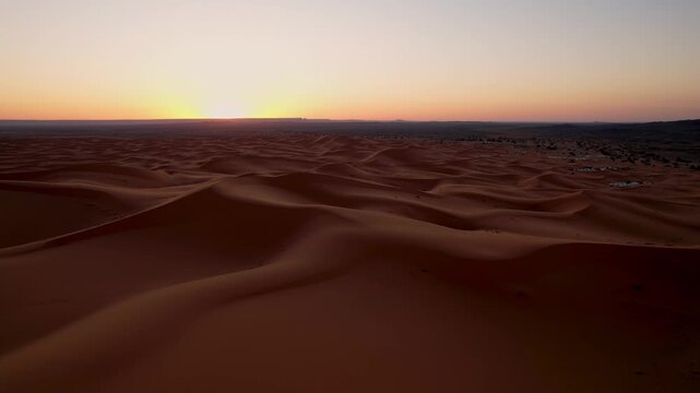 Erg Chebbi dune sea near Merzouga, Morocco, reveals endless wind sculpted formations and rich sandy textures illuminated by the first light of sunrise, slow drone forward flight shot.