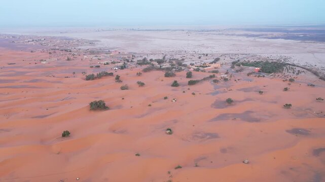 Drone aerial view of the edge of Erg Chebbi in Merzouga, where golden sand dunes meet the rocky desert, revealing the diverse landscapes of Morocco's Sahara.