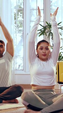 Indian Asian young couple learning yoga together in their lavish home, performing Parvatasana or seated mountain pose, focusing on alignment, posture, and inner balance in a peaceful environment