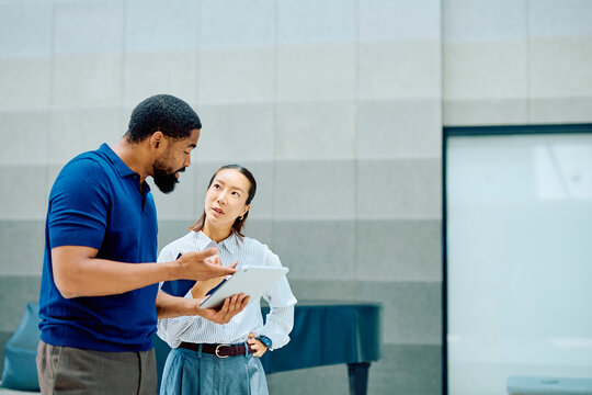 Two diverse business colleagues discussing a project plan, collaborating and communicating effectively with a digital tablet in a modern office