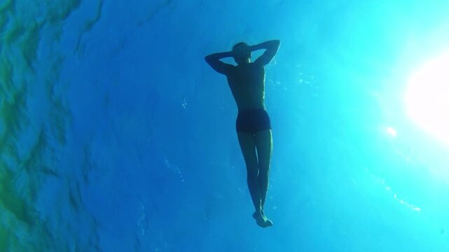 Relaxed man floating in the deep blue sea under the sun