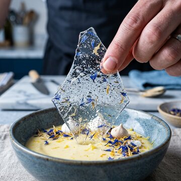 Chef placing floral sugar glass tuile into yellow custard dessert in professional kitchen
