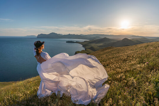 Woman dress mountain, woman in long white dress standing on coastal mountain during scenic golden sunset creating inspiring travel lifestyle vibes