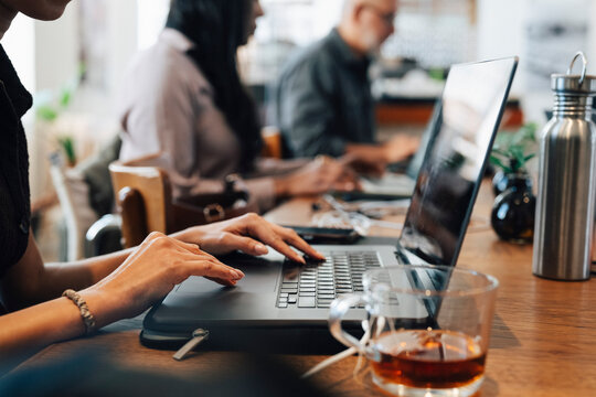 Close-up female freelancer working on laptop next to cup of tea at shared working desk