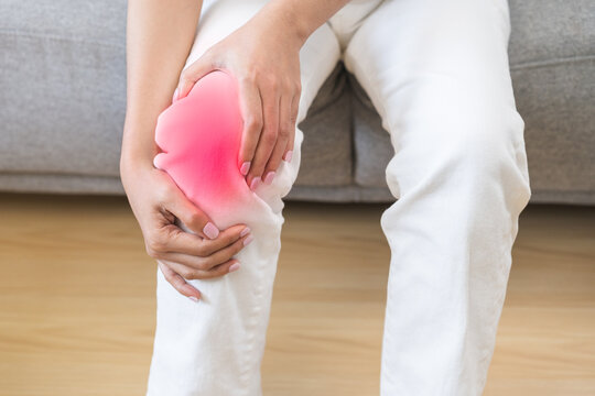 Health care of knee pain concept, close up hand of woman arthritis sitting joint ache, sore cramp or sprain tendon in leg on sofa at home. Osteoarthritis chronic disease of body problem from trauma.