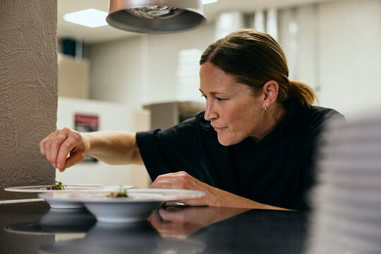 Professional female chef garnishing food dishes under heat lamp