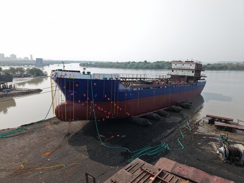 Targhar, Maharashtra, India - 23 December 2025: Aerial view of the Maldar Shipyard featuring a newly constructed cargo ship decorated with colorful ribbons resting on the riverbank.