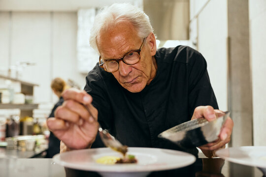 Dedicated senior male chef focusing on food plating and culinary presentation in restaurant kitchen