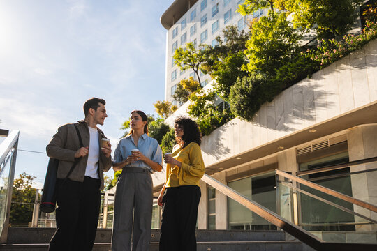 Three business colleagues standing outdoors, having coffee, and discussing during a break