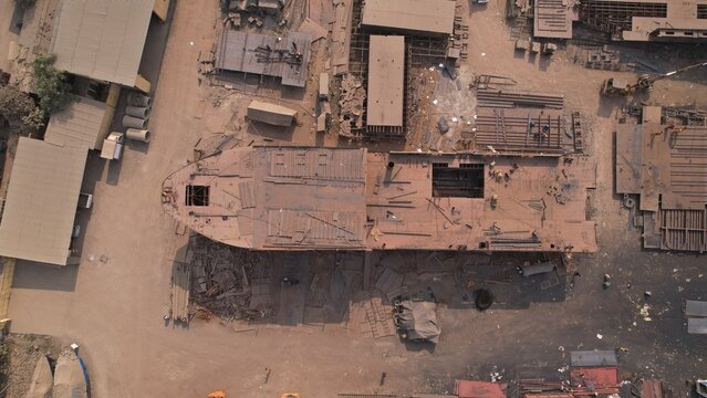 Targhar, Maharashtra, India - 23 December 2025: Aerial view of Maldar Shipyard showing industrial ship construction with metal hulls, scattered building materials, and workers.