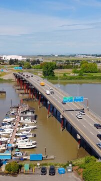 Richmond, British Columbia, Canada - An Aerial View of a Bridge Crossing a River Beside a Marina with Docked Boats, Surrounding Roadways, and Airport-area Landscapes - Vertical Shot