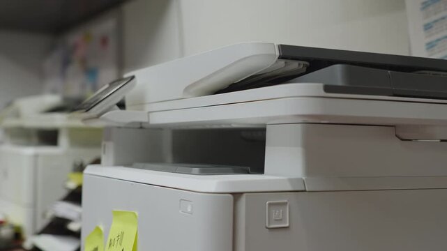 An office worker removes freshly printed paperwork from a fax printer during a routine business task. Ideal for administration, office workflow, communication, and document management themes.