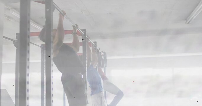 Three men reaching up and gripping rig, backlit gym, doing pull-up reps for strength ending hang