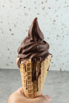 A view of a hand holding chocolate dipped frozen yogurt in a waffle cone.