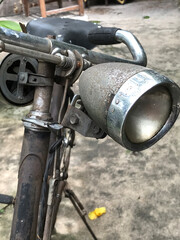 Close-up of an old vintage bicycle headlight, handlebar, and classic rod brake mechanism with a weathered, rusty finish. © bowee