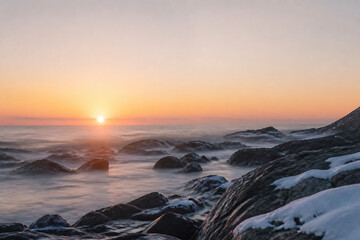 Fototapeta premium A serene sunrise over a rocky coastline with gentle waves washing ashore.