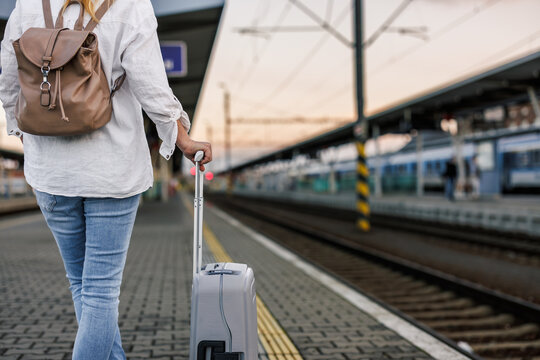 Woman tourist with suitcase and backpack waiting for train at railway station platform. Solo travel concept