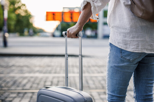 Woman traveler with suitcase is checking arrival and departure board schedule timetable at bus station. Solo travel concept