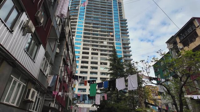 Colorful laundry hanging on clotheslines to dry between an old residential building and a modern skyscraper, representing the urban contrast and daily life in a developing city district