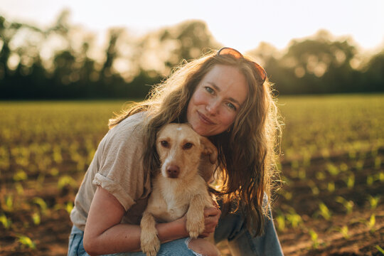 Woman hugging pet dog in a rural field at sunset