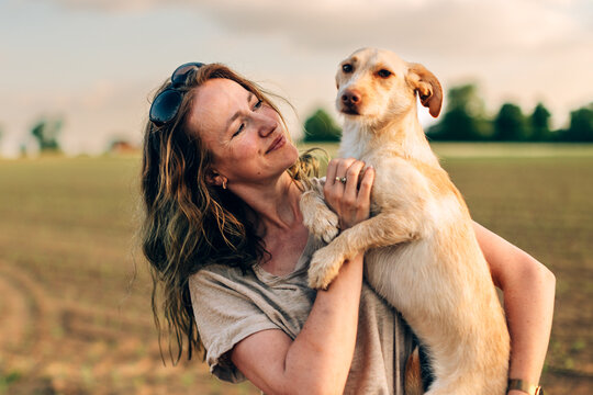 Woman holding dog in field enjoying sunset light
