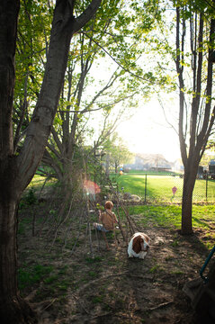 Young boy and basset hound dog in a backyard stick fort