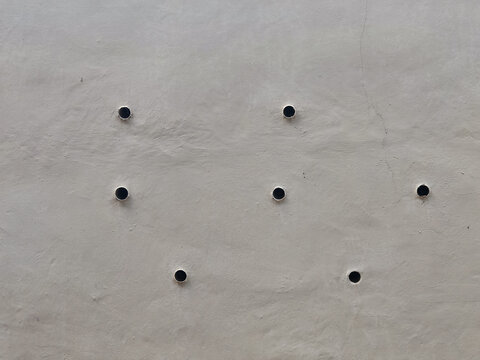 High-angle abstract shot of a textured gray cement wall featuring a geometric pattern of circular drainage hole. Ideal for clean industrial backgrounds, architectural templates, architectural engineer