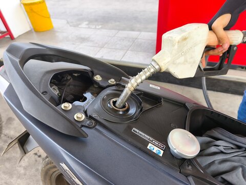 Close-up of a gas station attendant filling up a motorcycle's fuel tank with a petrol nozzle at a public refueling station (Pertamina).