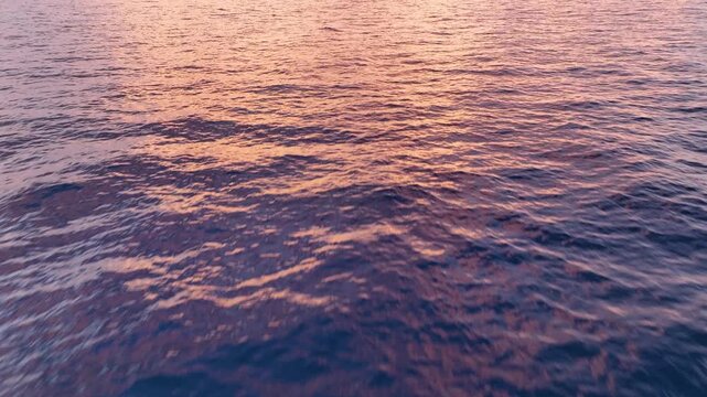 Calm water surface reflects pink and orange hues during sunset over the ocean