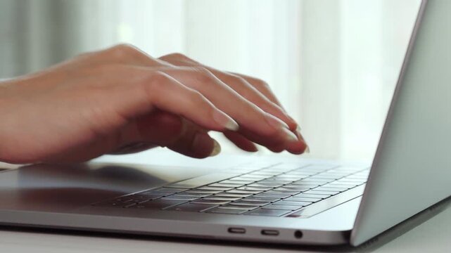 Hands type on laptop keyboard. Fingers press keys with precision. Soft natural light streams through window. Scene suggests focused, productive work. Ideal for business, education