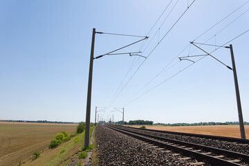 Electrified railway tracks stretching into the distance across rural farmland. Strong perspective for transportation and infrastructure themes. © Eric