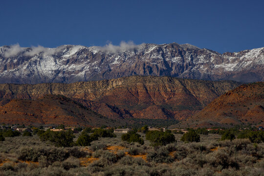 A suburban desert community sits at the base of layered red cliffs beneath a massive snowy mountain.